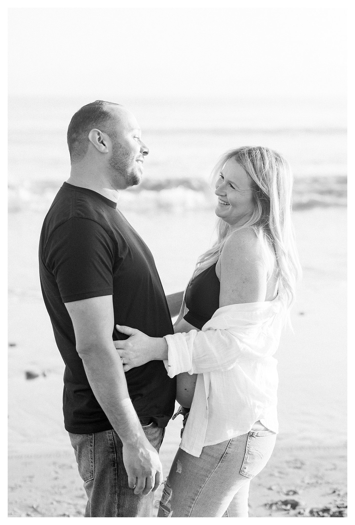 A pregnant couple smiling at each other at the beach in Malibu, Ca.