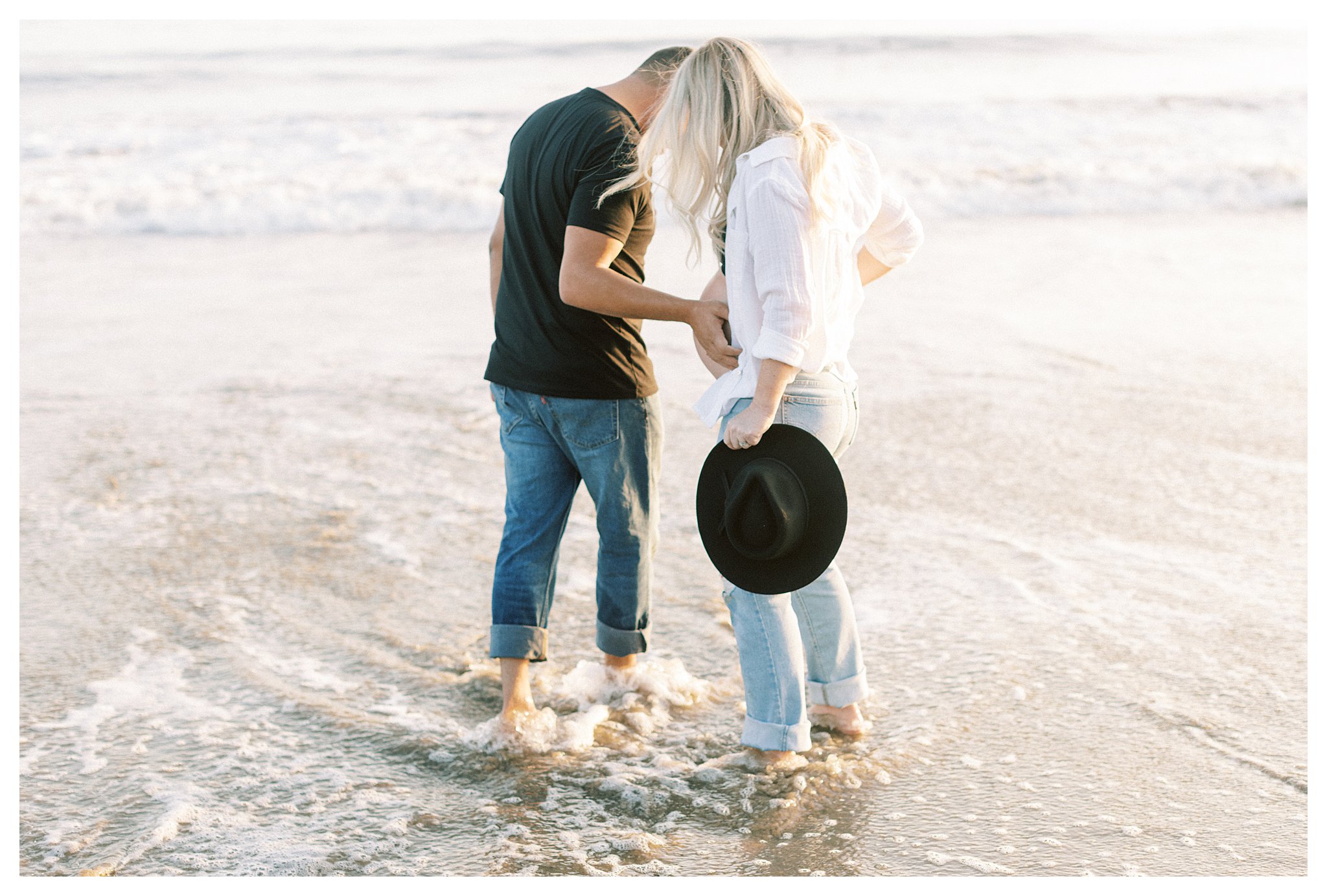 A couple walking along the beach with dad to be's hand on mom's belly.  