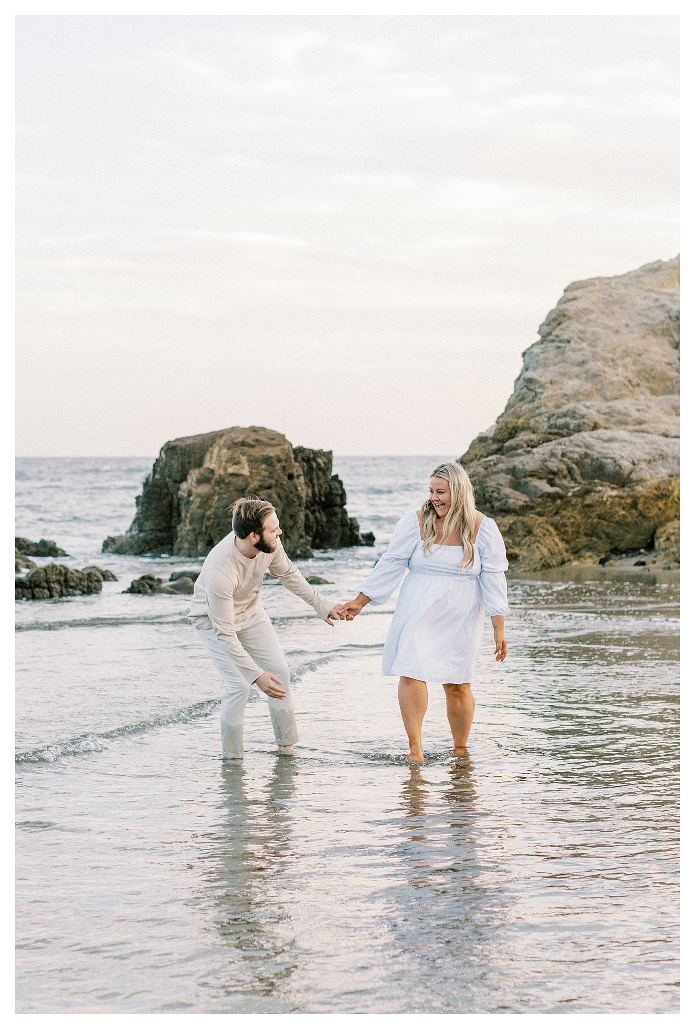 The engaged couple splashing each other with water at Leo Carrillo beach in Malibu, Ca.