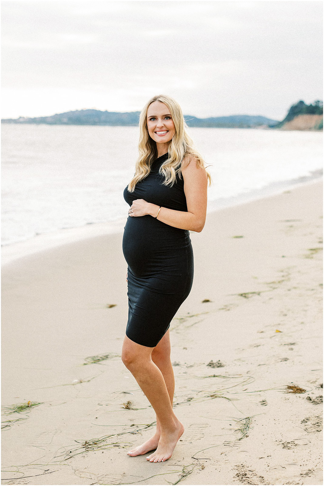 A pregnant mom to be standing on the beach.  