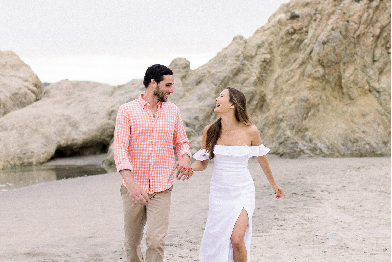 An engaged couple running along the sand at Leo Carrillo, Ca in Malibu, Ca.