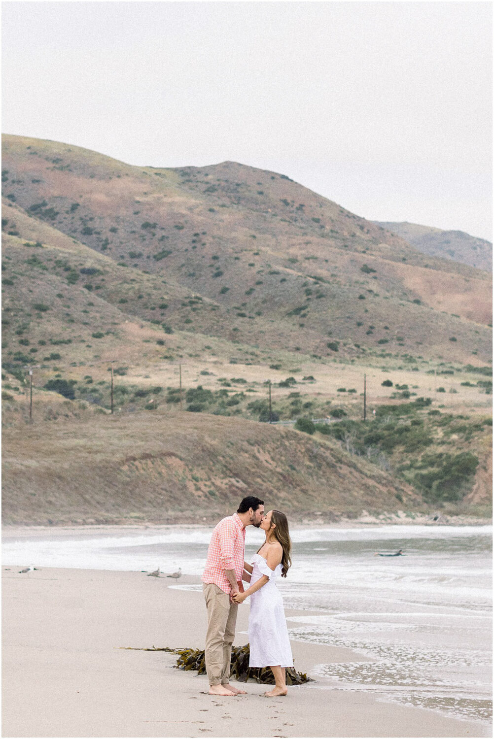 A couple kissing on the beach in Malibu, Ca with the Santa Monica Mountains in the background.  