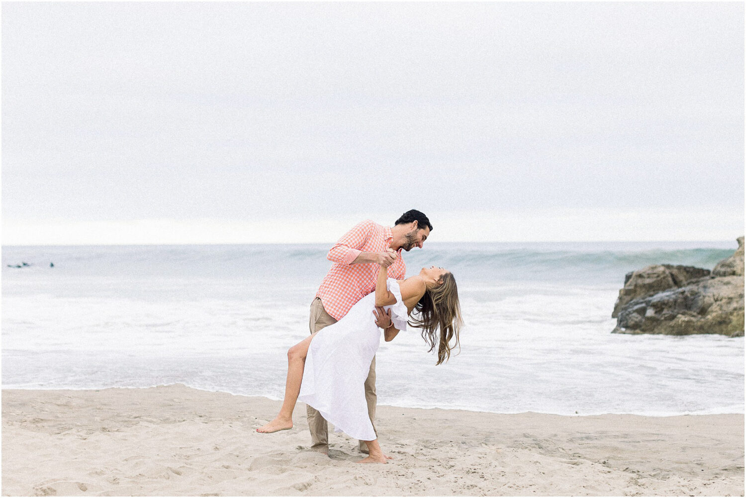 A man dips his fiance in front of the ocean at Leo Carrillo Beach.