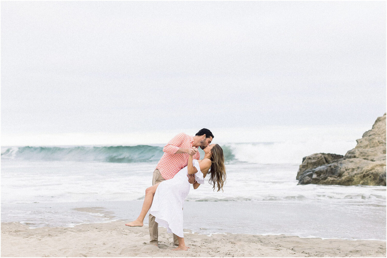 An couple kisses during a dip in front of the pacific ocean in Malibu, Ca.