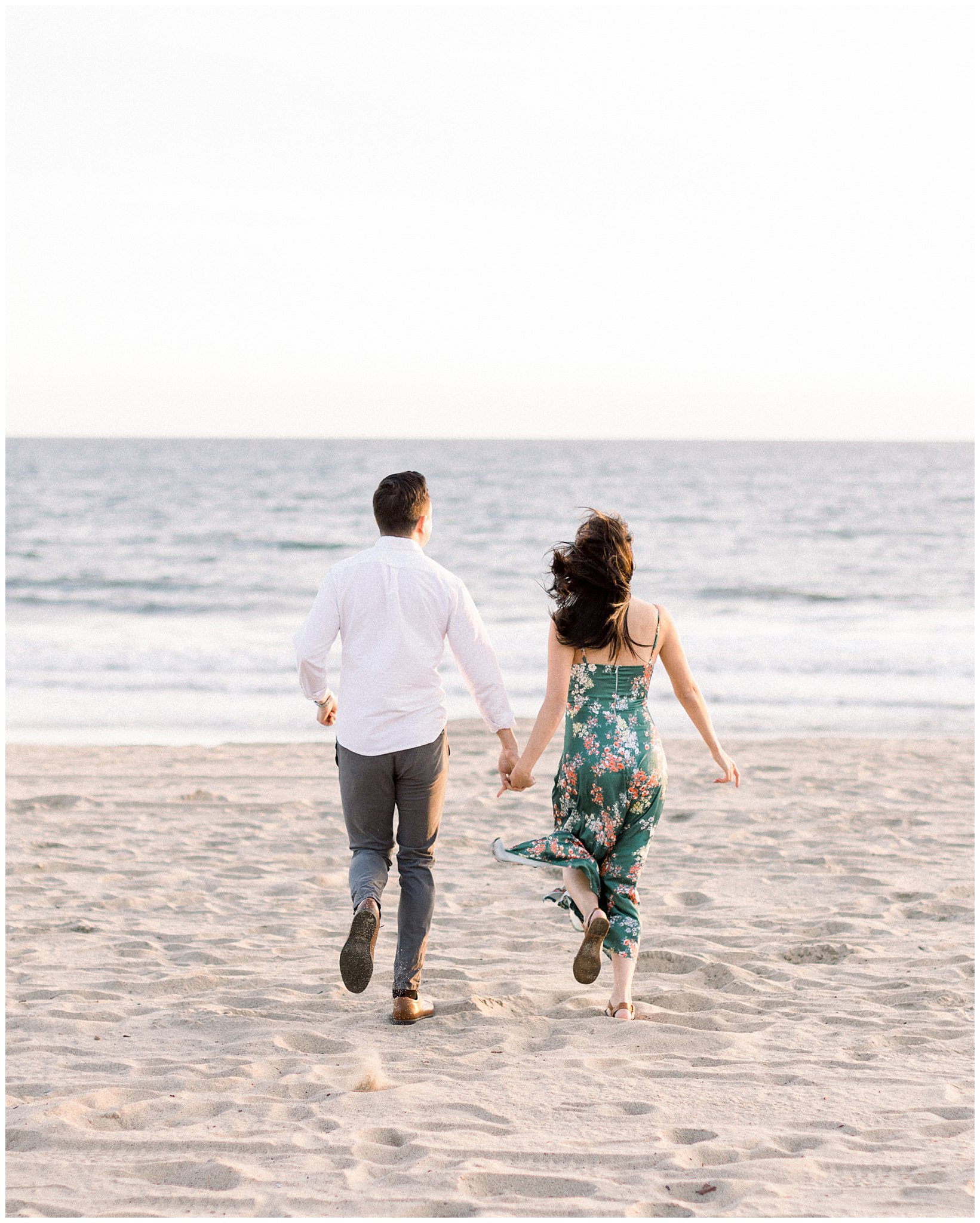 A couple playfully jogging hand in hand in the sand at Will Rogers Beach in Pacific Palisades.