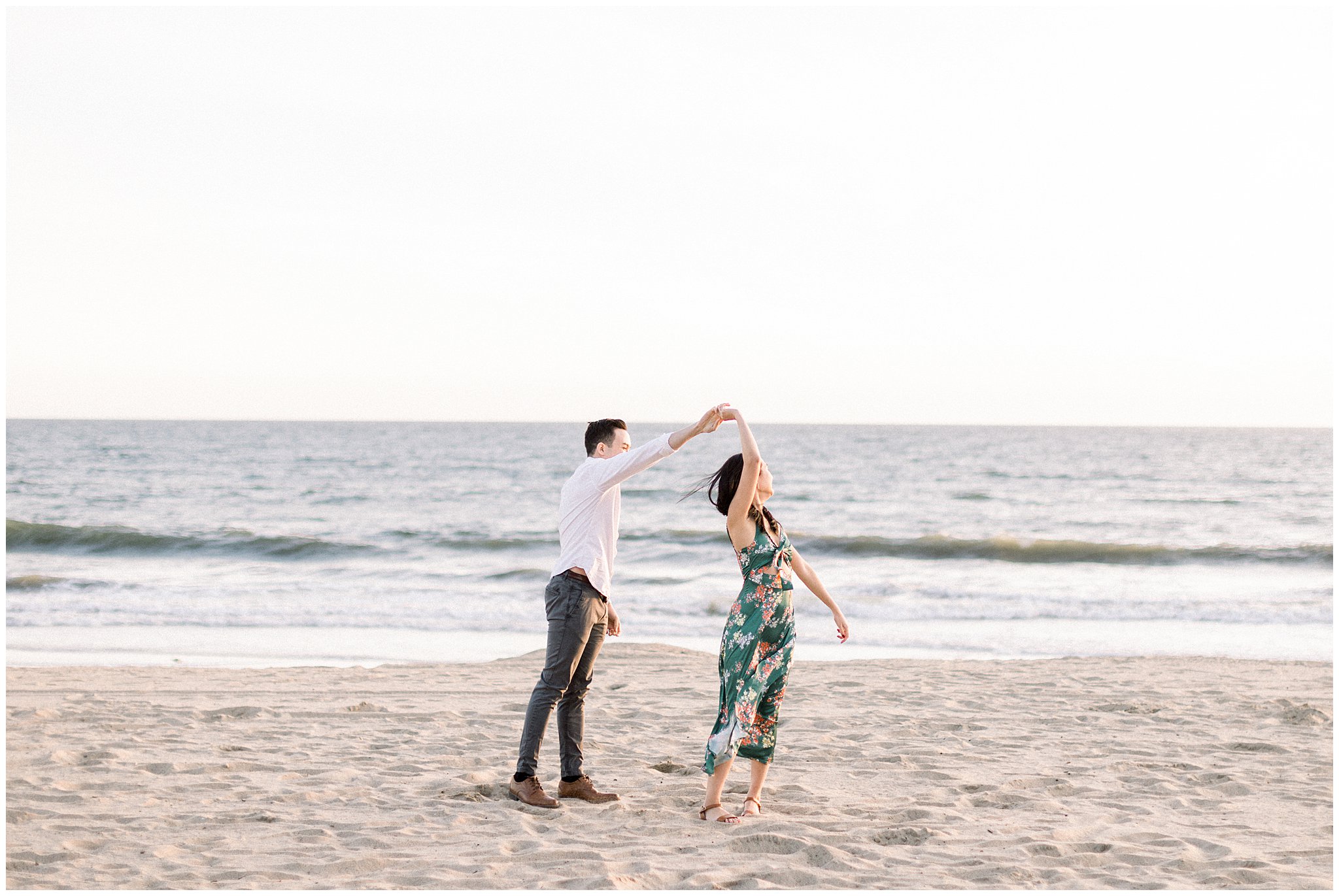 An engaged couple playfully twirling on the sands of a Santa Monica beach.  