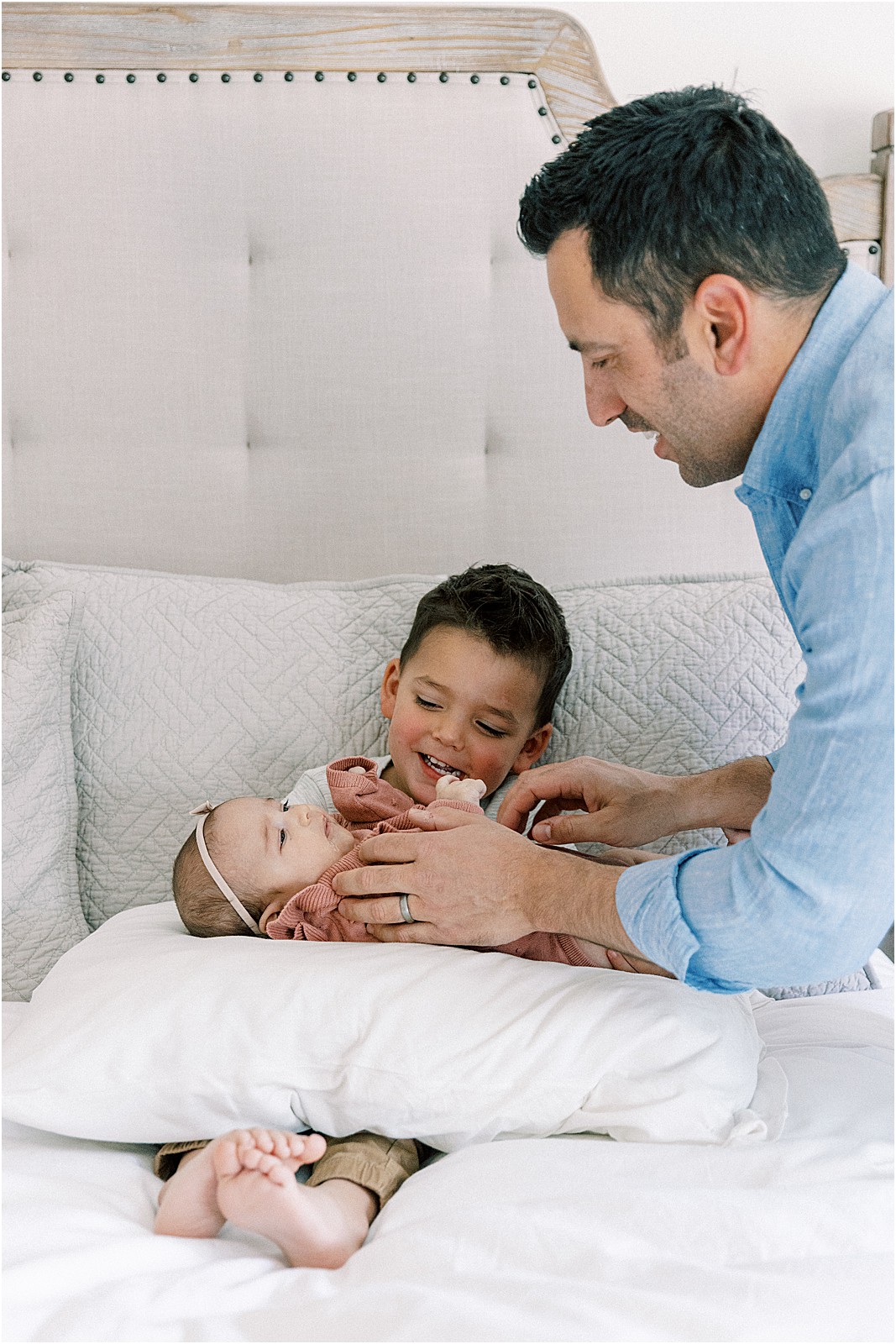 Dad helping big brother hold new baby carefully during family photo session.