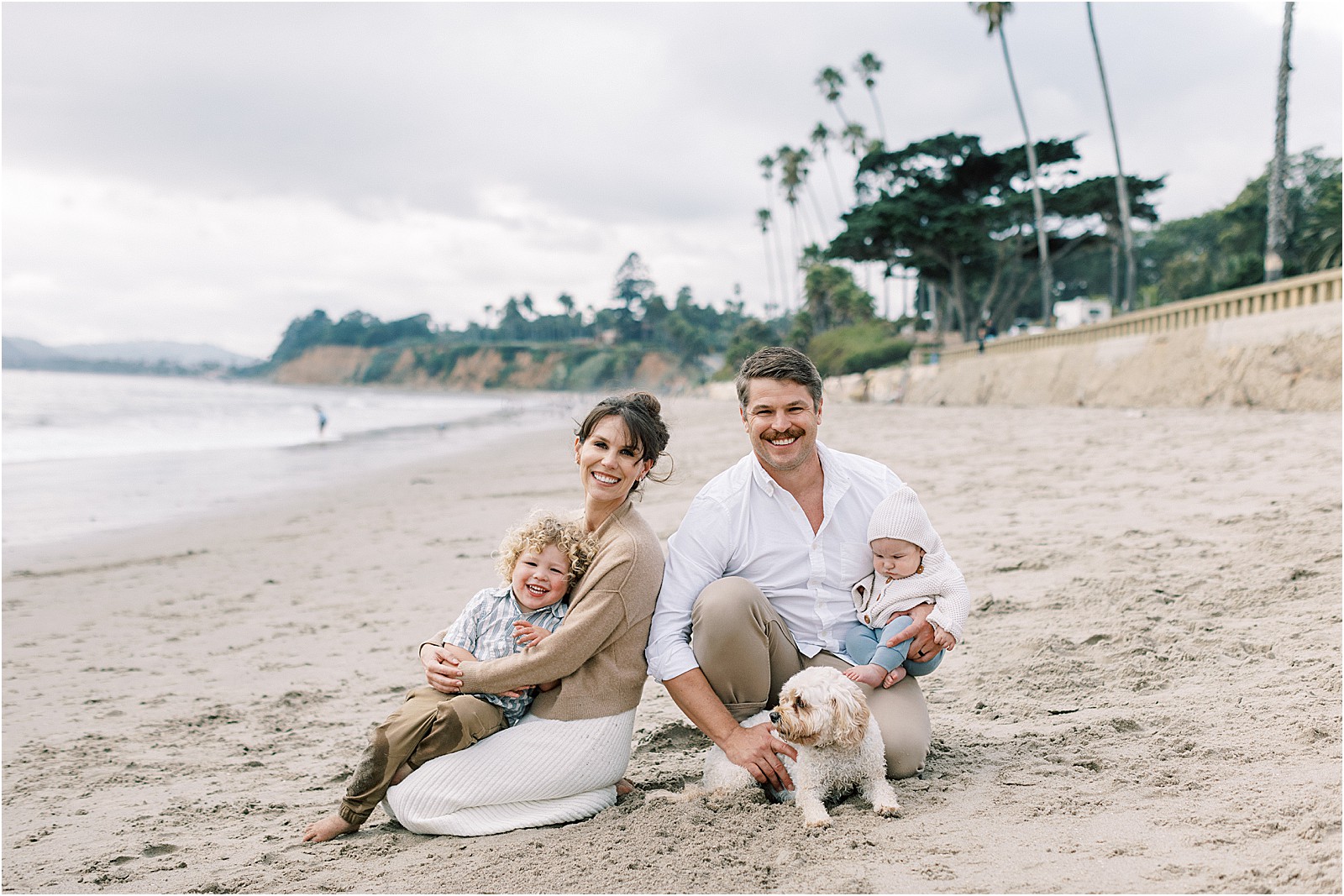 Parents hugging children with moody clouds in the background at Butterfly Beach