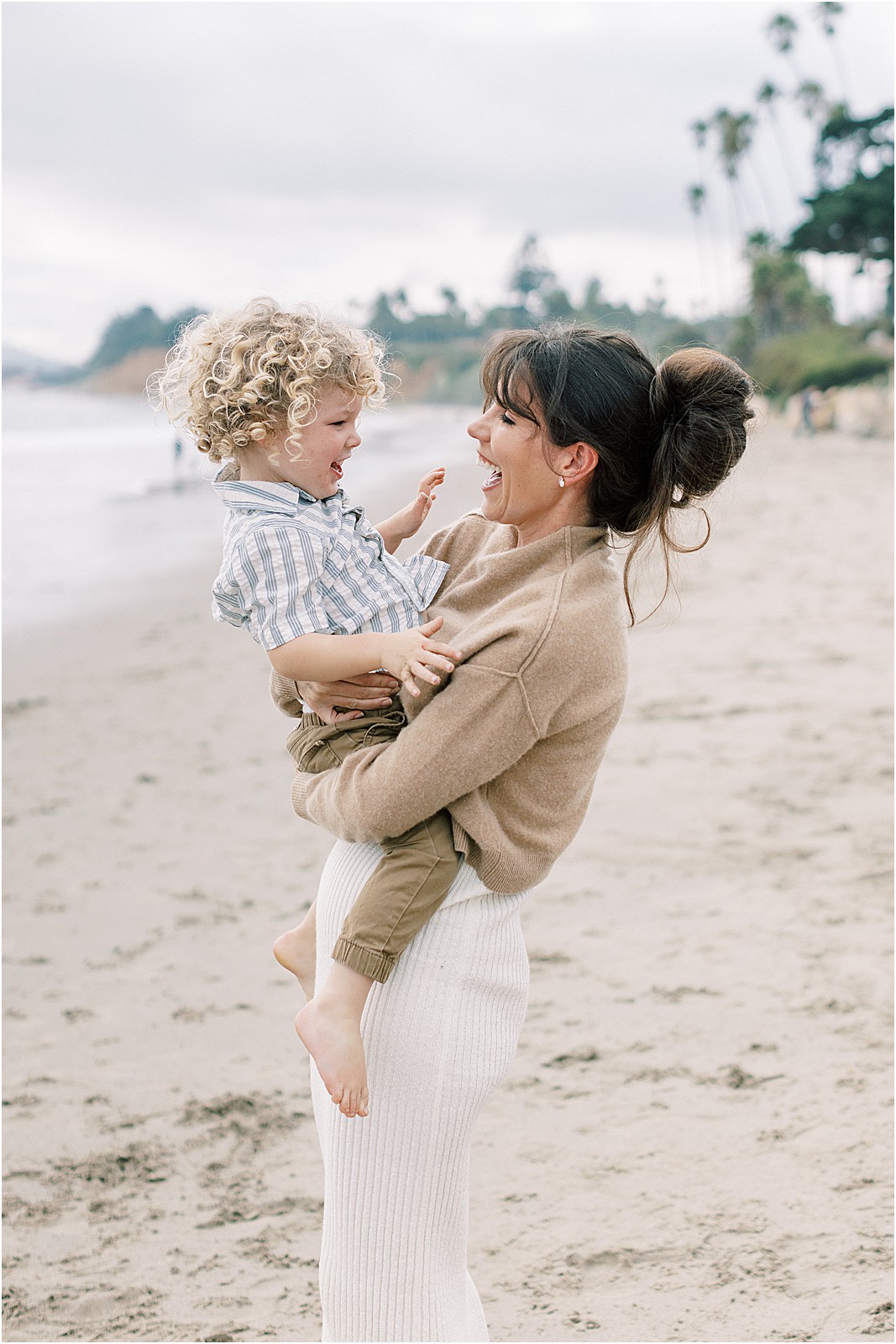 Vertical shot of mom holding toddler while standing in the sand at Butterfly Beach