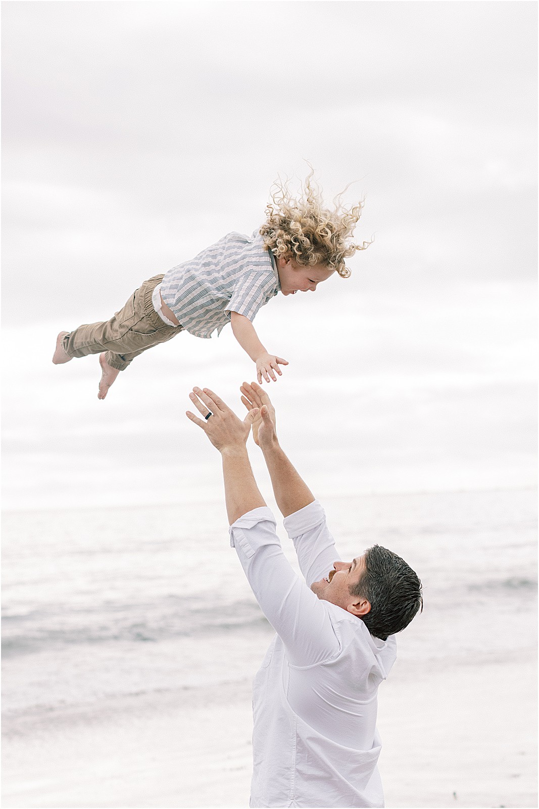 Dad tossing child in the air during an overcast family photo shoot in Montecito