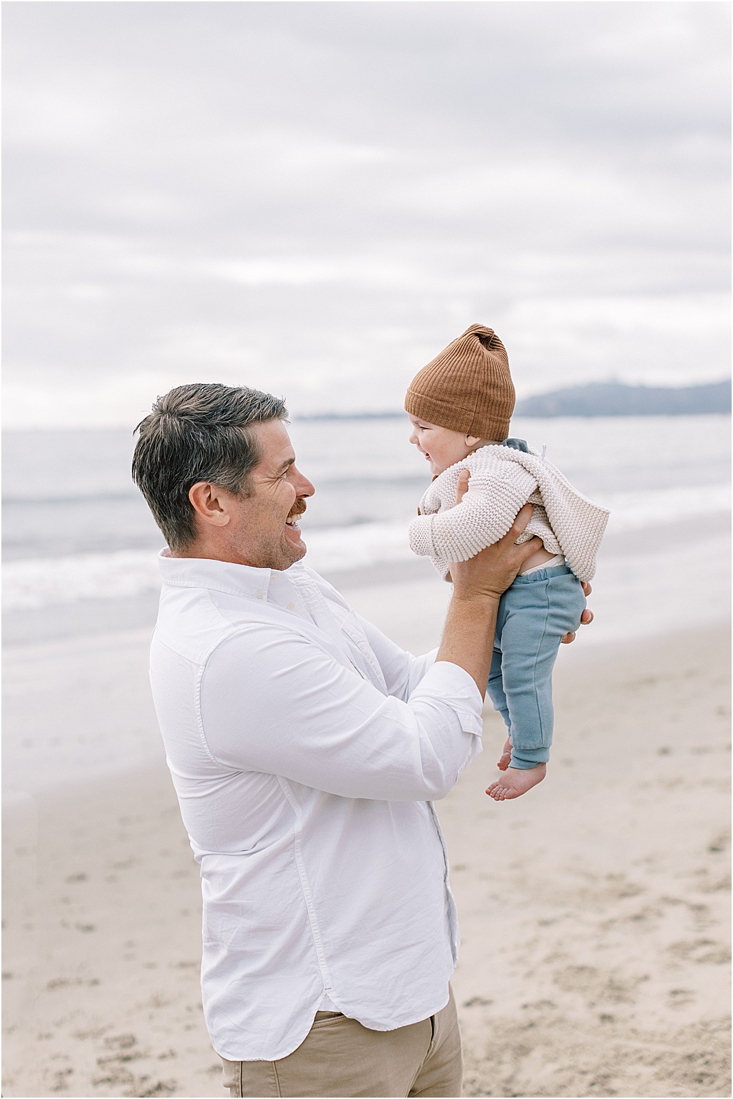 Dad holding up newborn in the air during an overcast family session in Montecito