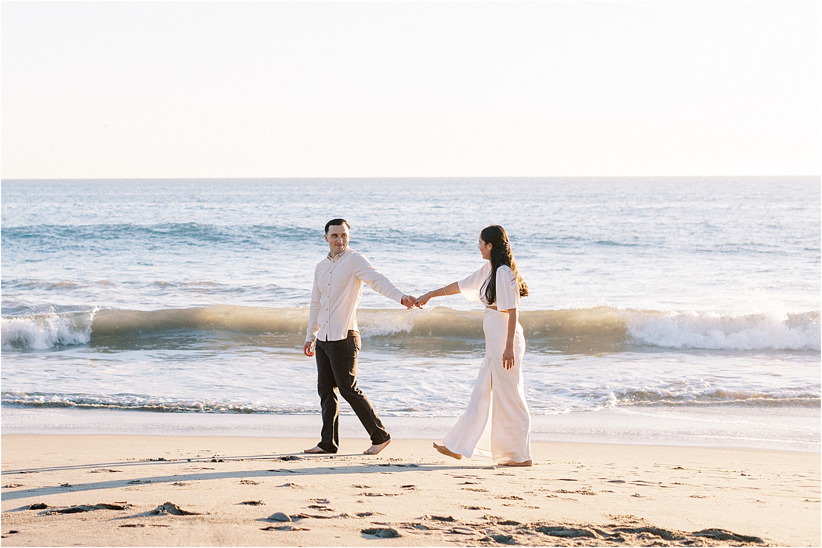 Candid smiles as couple walks barefoot through the sand in Malibu.