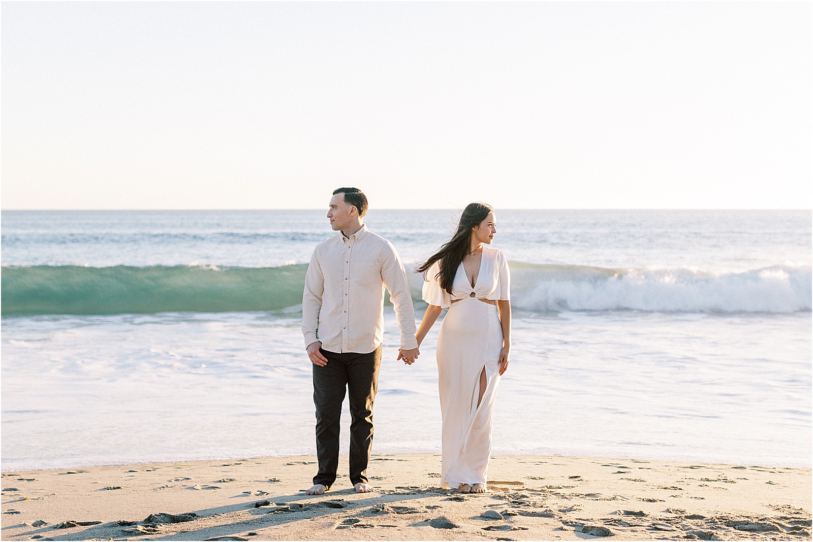 Editorial-style engagement portrait of couple framed by coastal waves in Malibu