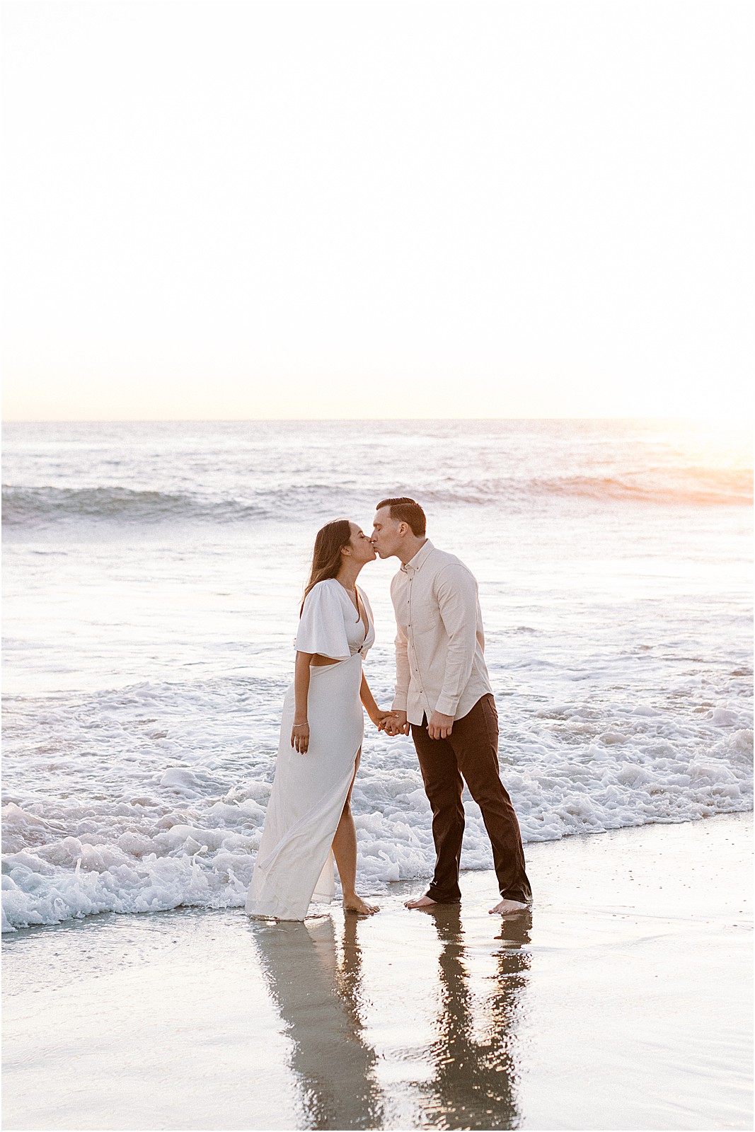 Warm, glowing light behind couple as they share a kiss during sunset engagement photos in Malibu.