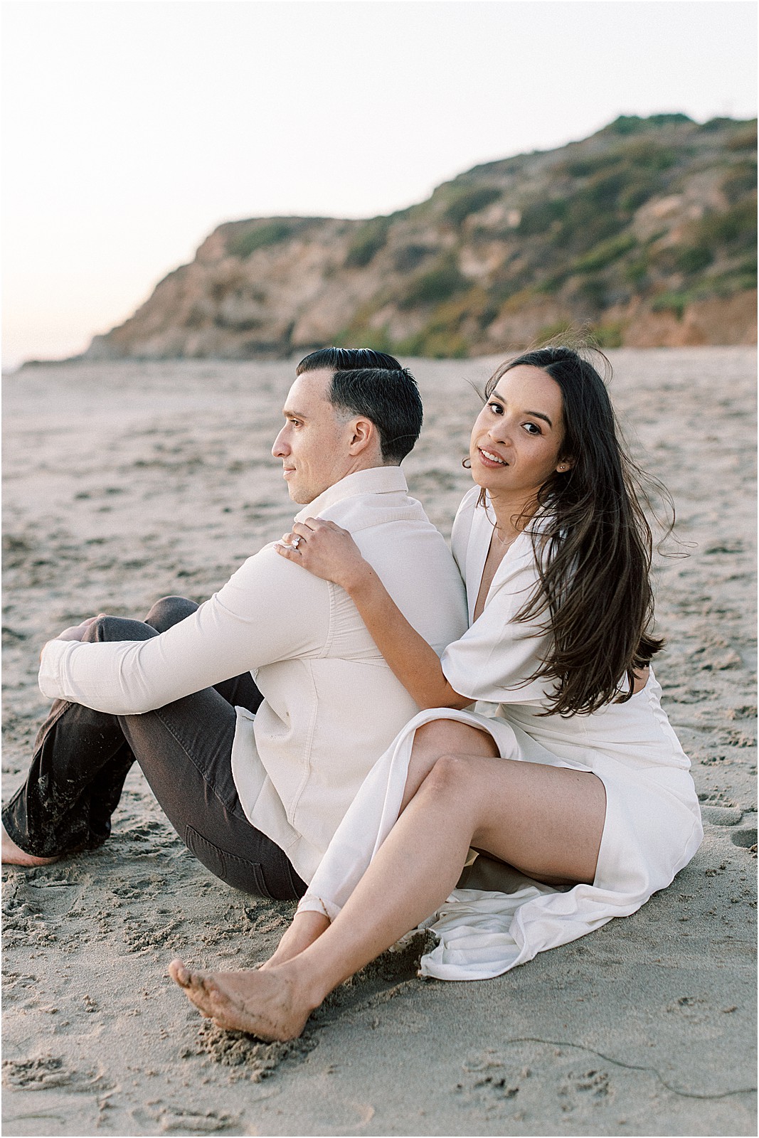 Bride looking at camera while embracing groom during engagement photos in Malibu