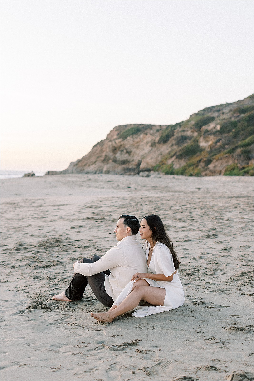 Romantic moment as couple sits facing the water during golden hour in Malibu.