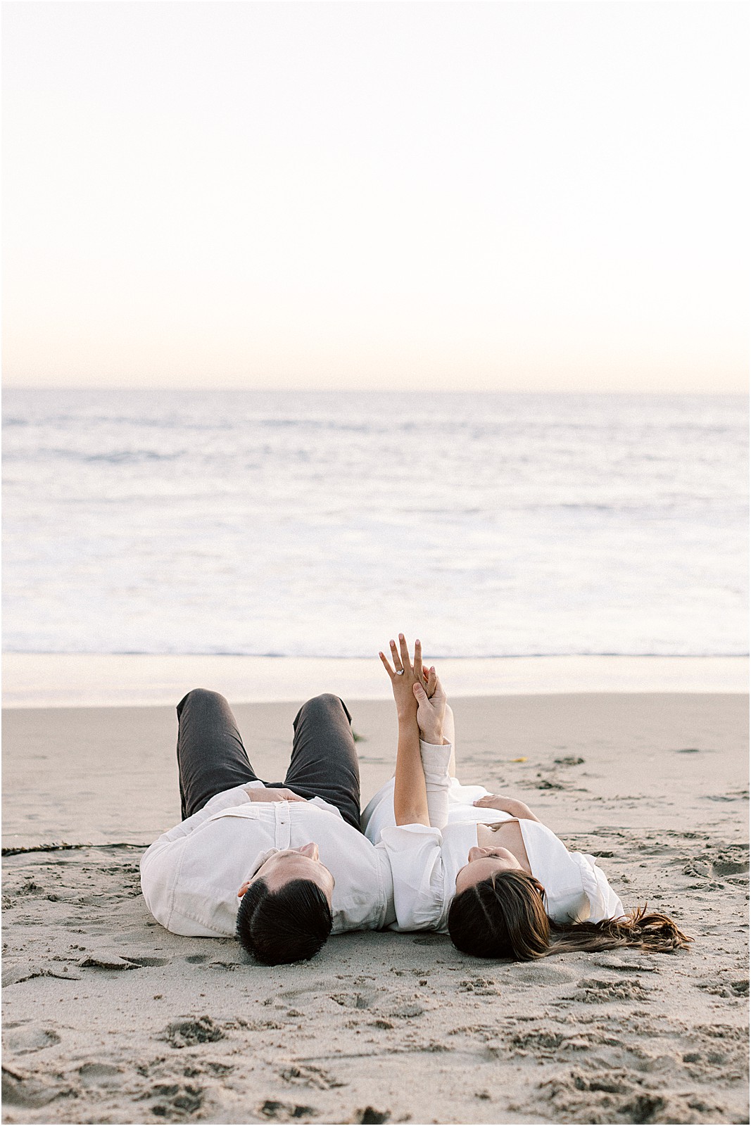 Couple laying side by side holding hands as the tide comes in at Leo Carrillo Beach.