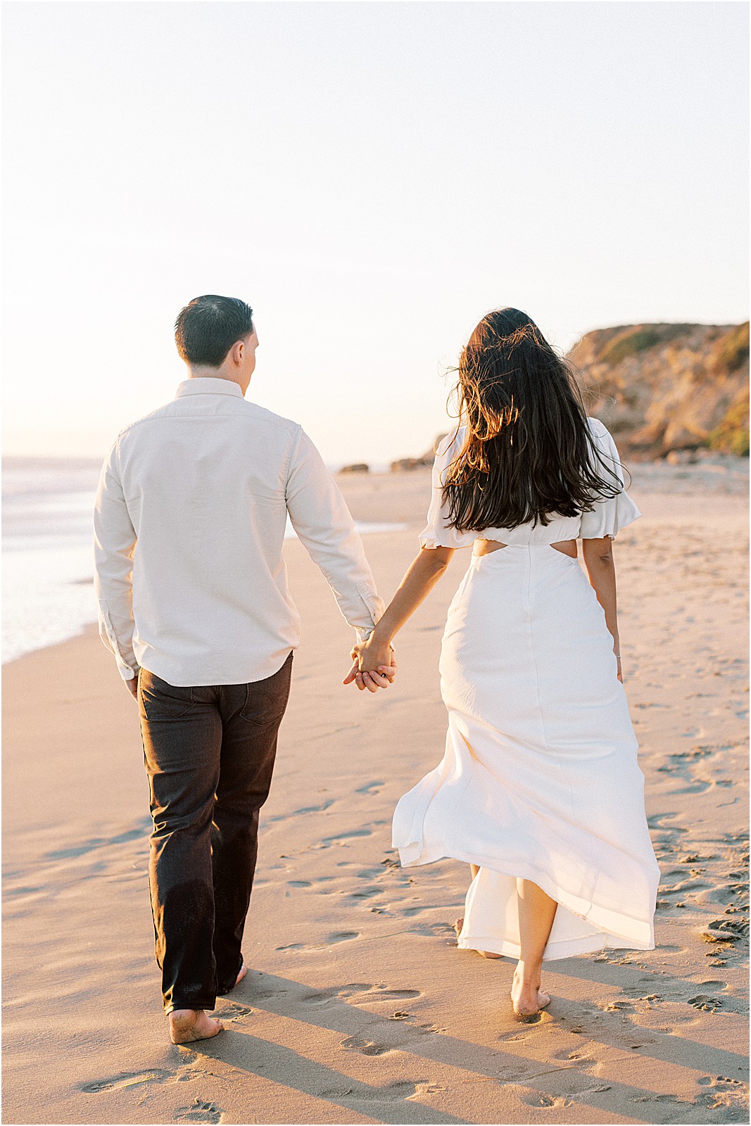 Couple walking hand in hand during a pink golden hour in Malibu.