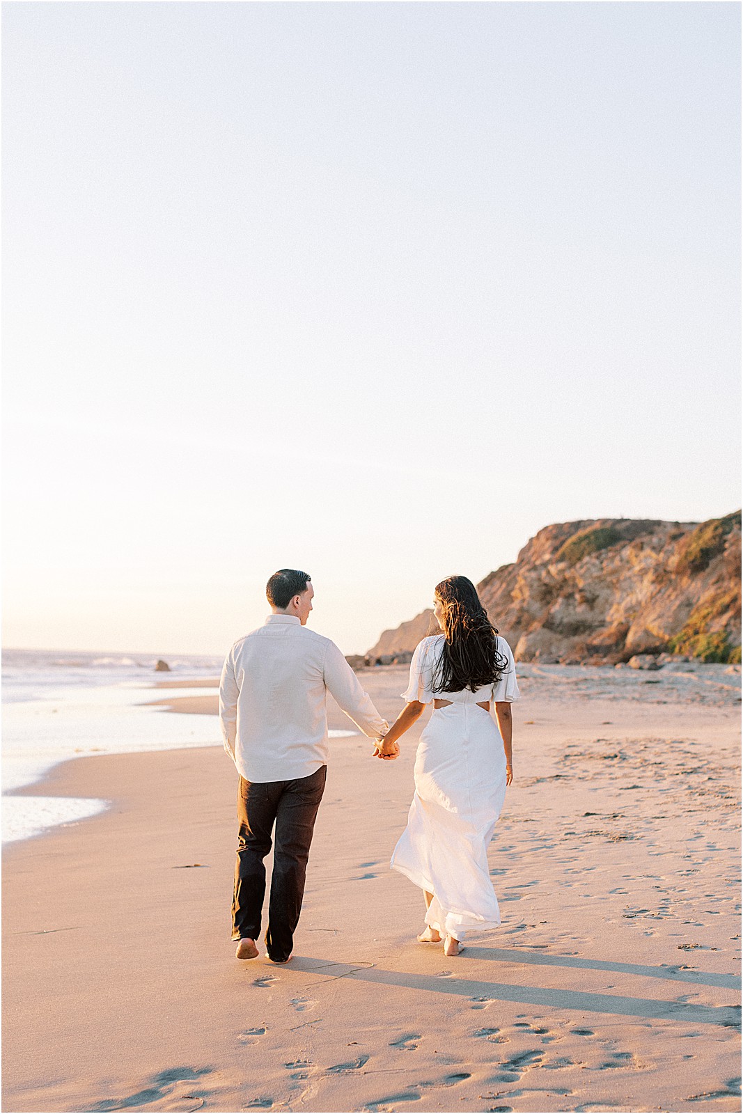 Candid photo of couple walking barefoot along shoreline at Leo Carrillo Beach
