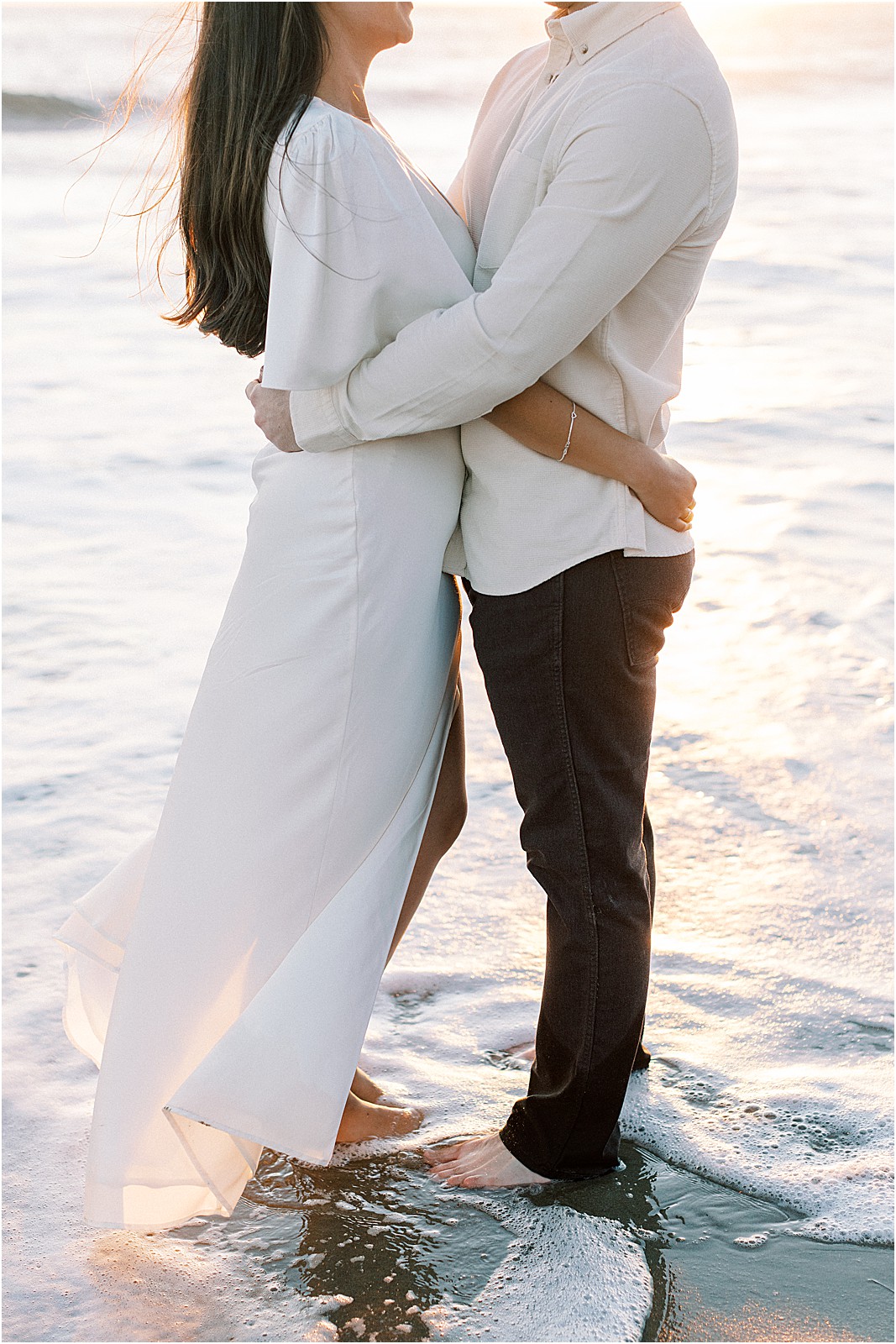 Couple embracing while standing in the water during engagement session.