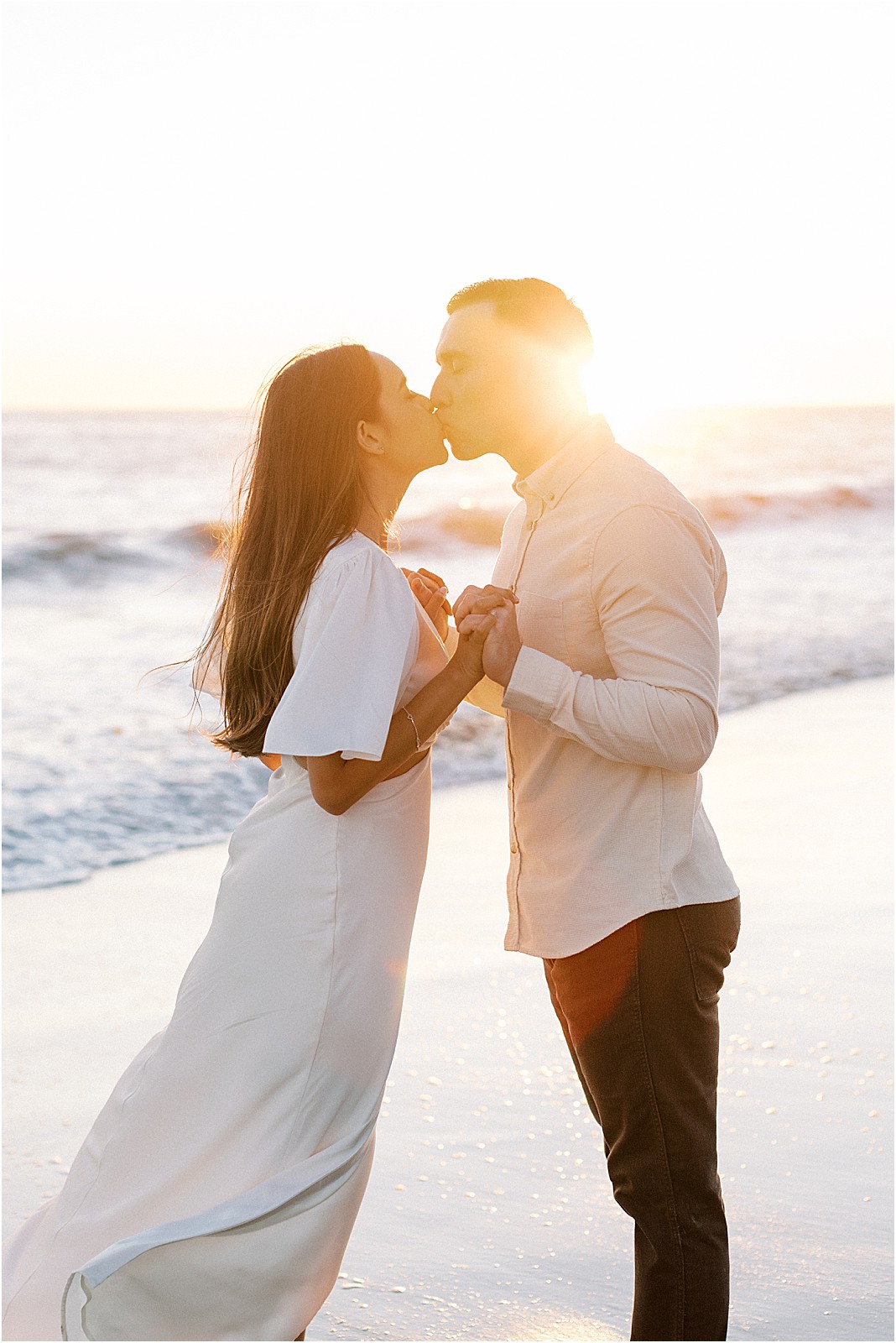 Couple holding hands with golden sunset behind them in Malibu.