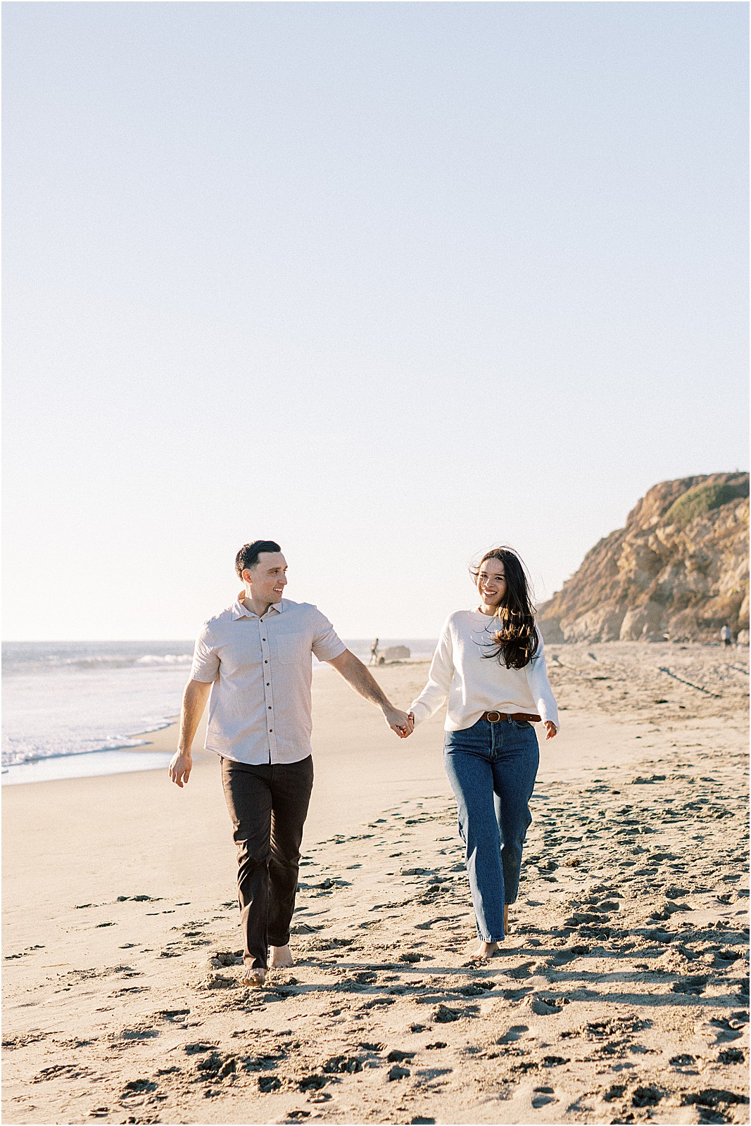 Couple jogging hand in hand along Leo Carrillo Beach during their engagement session