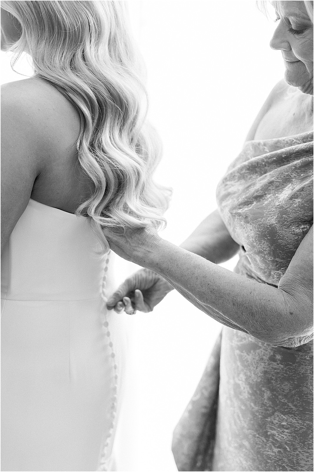 mother of the bride helping bride into wedding dress