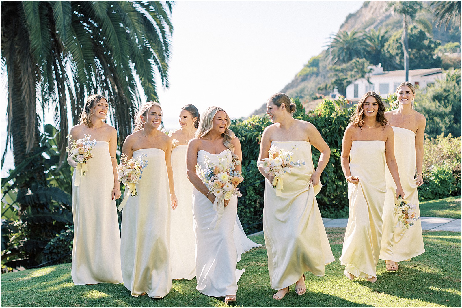 bride surrounded by her bridesmaids in pale yellow dresses walking on lawn at bel air bay club